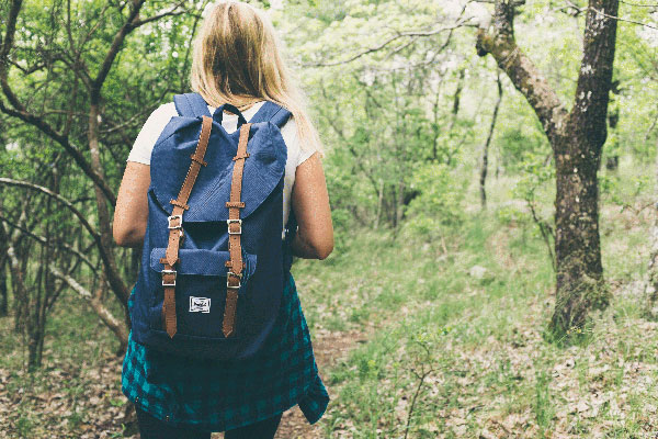 Una camminatrice con lo zaino lungo un sentiero fra gli ulivi